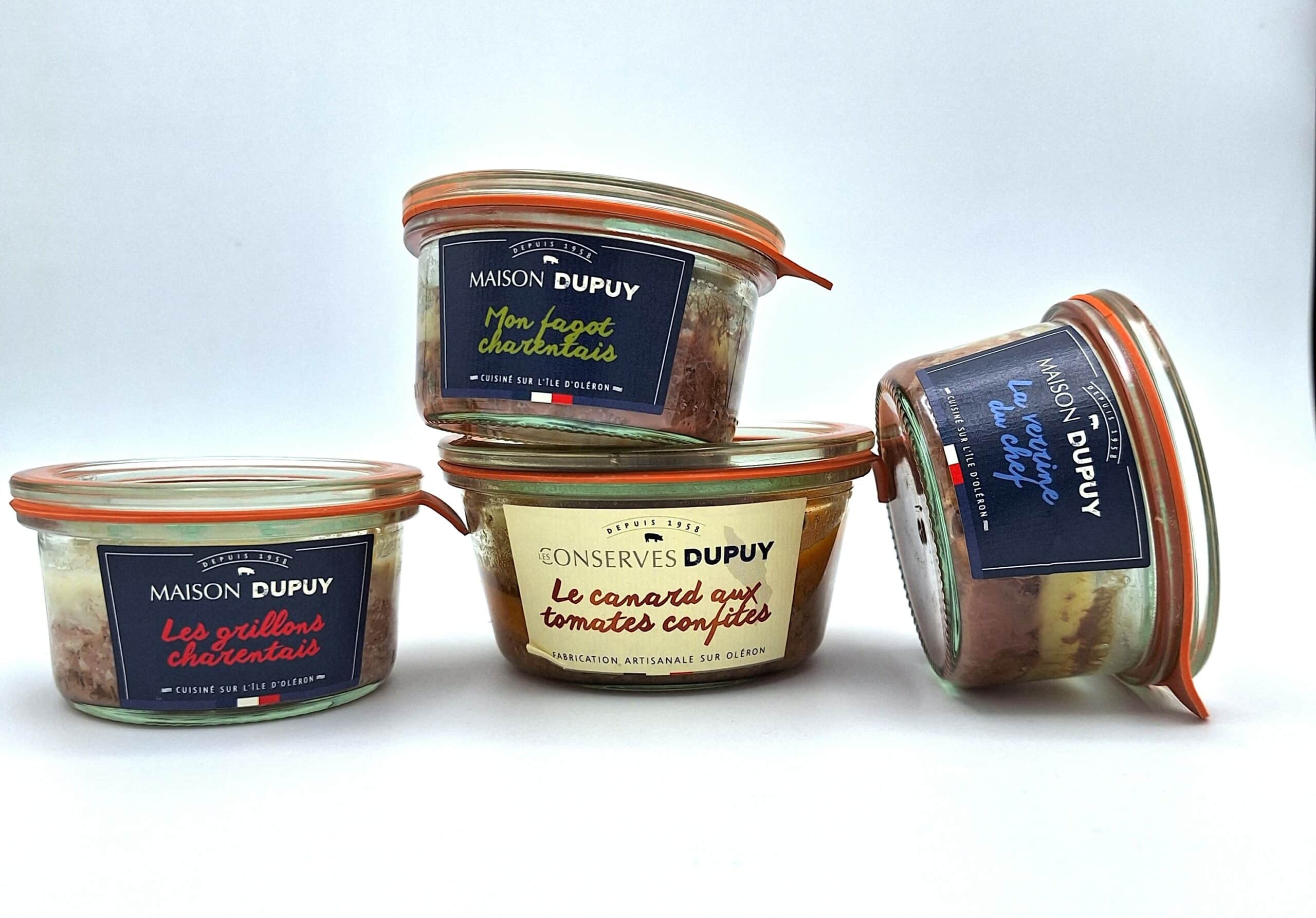 Quatre bocaux de conserves françaises sont astucieusement disposés, mettant en valeur diverses variétés comme « Les Grillons Charentais » et « Le Canard Aux Tomates Confites ». Étiquetés sous « Maison Dupuy » et « Conserves Dupuy », ces Trésors Gastronomiques proviennent de la prestigieuse région de Marennes.